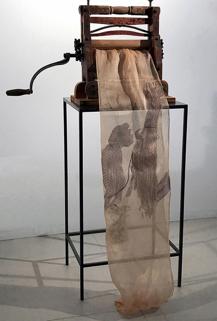 Antique laundry wringer on metal stand with printed silk fabric.