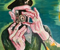 Older white male wearing a beret holding a camera in fron tof his eyes, taking a picture.