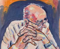 Older white male in thought, sitting in a chair, elbows on table, hands crossed in front of him.